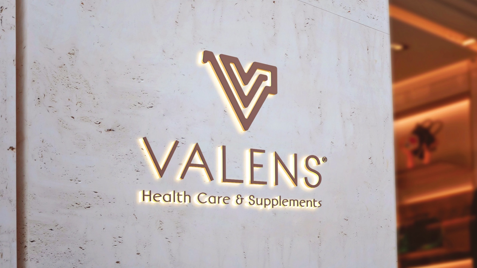 Valens logo in illuminated gold on a travertine wall